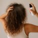 imagen generada por ia Melena rizada con frizz mientras una mujer aplica spray con la mano, ejemplo de rutina rápida para definir rizos en poco tiempo