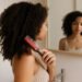 imagen generada por IA – mujer con rizos tipo 3 o 4 peinando su melena con cepillo tipo Denman frente a espejo, en baño neutro con luz natural
