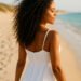 imagen generada por IA de una mujer con rizos definidos caminando por la playa con un vestido blanco ibicenco, representando una rutina curly ligera en verano