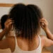generada por ia mujer con cabello rizado en transición, mostrando raíces definidas y puntas alisadas, frente al espejo en entorno cálido
